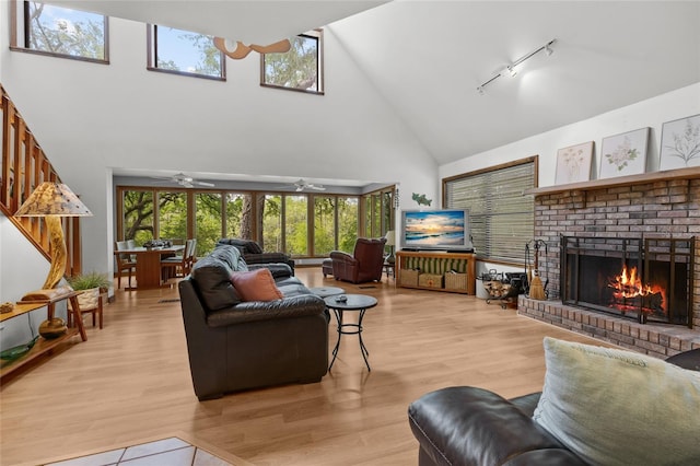 living area with light wood finished floors, rail lighting, a fireplace, high vaulted ceiling, and ceiling fan