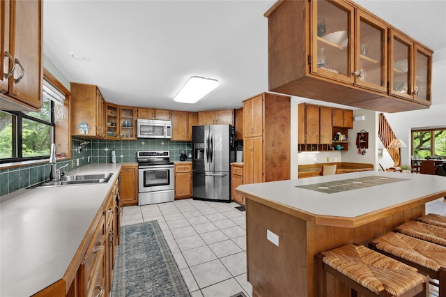 kitchen with stainless steel appliances, light tile patterned floors, a sink, decorative backsplash, and brown cabinetry