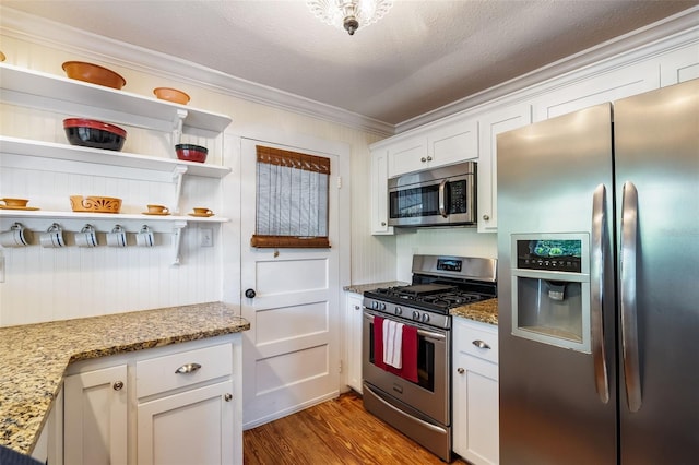 kitchen with wood finished floors, stainless steel appliances, white cabinetry, ornamental molding, and light stone countertops