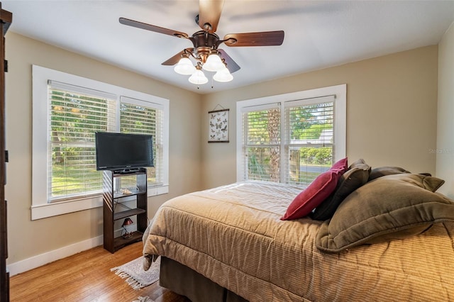 bedroom with a ceiling fan, light wood finished floors, baseboards, and multiple windows