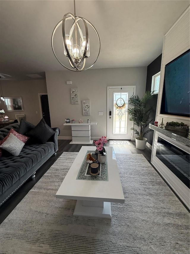 living room with a glass covered fireplace, an inviting chandelier, wood finished floors, and baseboards