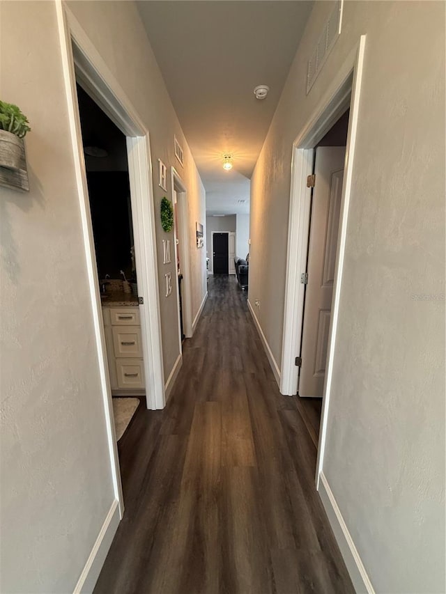 corridor with dark wood finished floors, visible vents, and baseboards