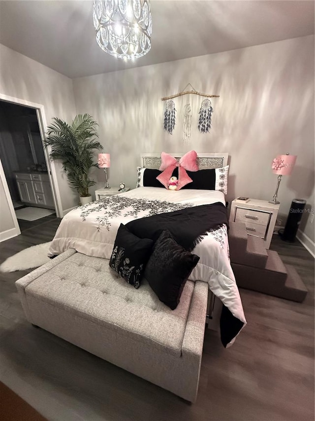 bedroom featuring baseboards, wood finished floors, an inviting chandelier, and ensuite bathroom