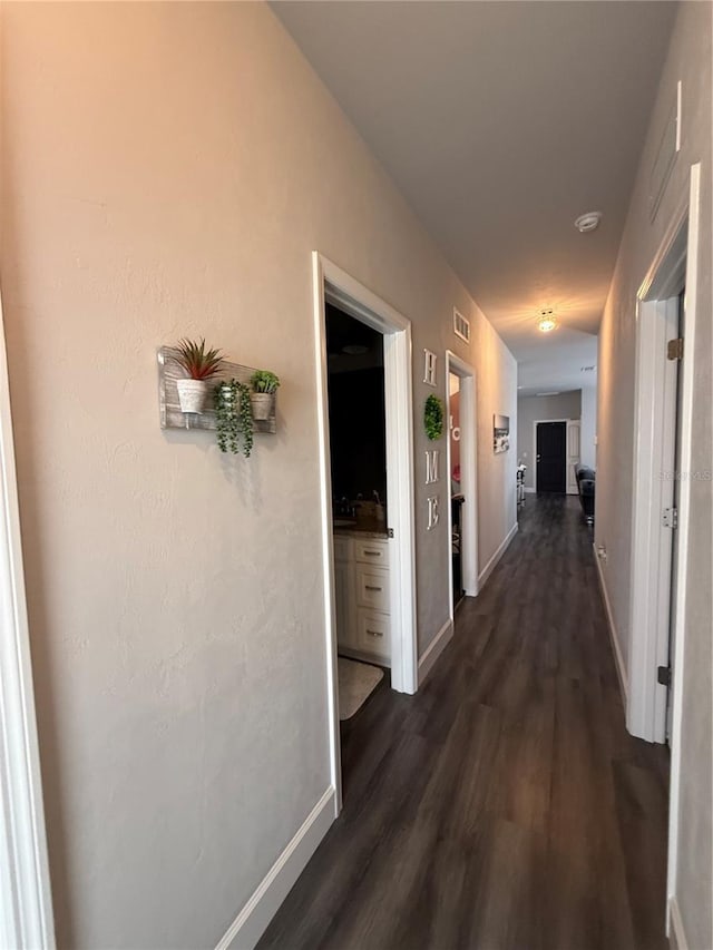 corridor featuring dark wood-style flooring, visible vents, and baseboards