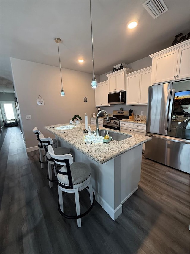 kitchen with dark wood-style flooring, a center island with sink, visible vents, white cabinets, and appliances with stainless steel finishes