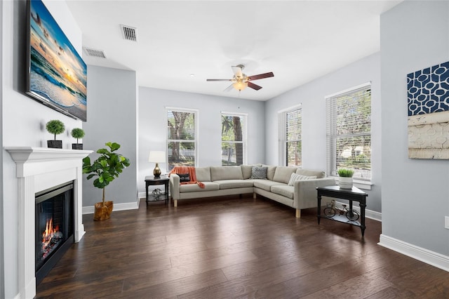 living area featuring a warm lit fireplace, a ceiling fan, baseboards, and hardwood / wood-style floors