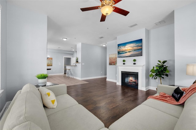 living room featuring a ceiling fan, a glass covered fireplace, wood finished floors, and baseboards