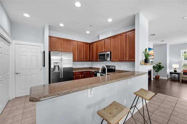 kitchen featuring stainless steel appliances, light tile patterned floors, a peninsula, a kitchen breakfast bar, and recessed lighting
