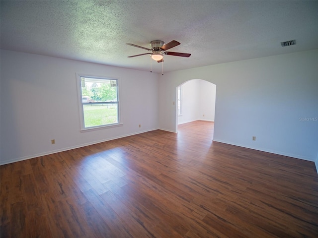 empty room featuring arched walkways, ceiling fan, visible vents, and dark wood finished floors