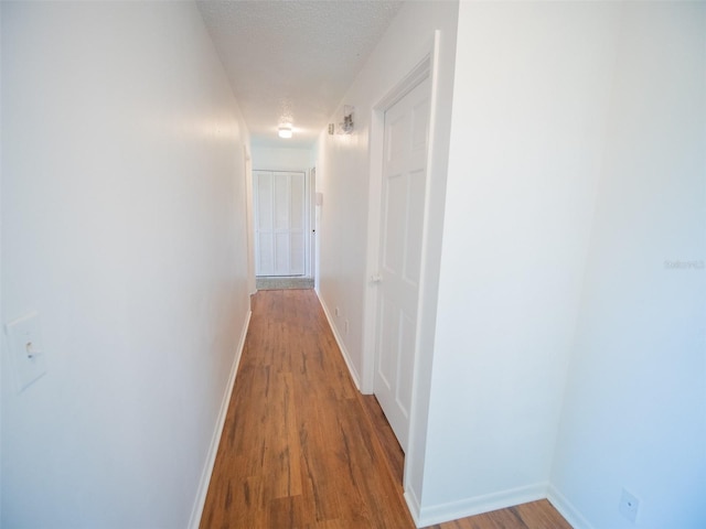 hall featuring baseboards, a textured ceiling, and wood finished floors