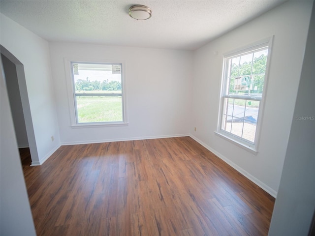 empty room with arched walkways, baseboards, dark wood finished floors, and a healthy amount of sunlight