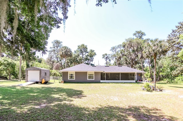 back of property with fence, a detached garage, a lawn, a storage unit, and a sunroom