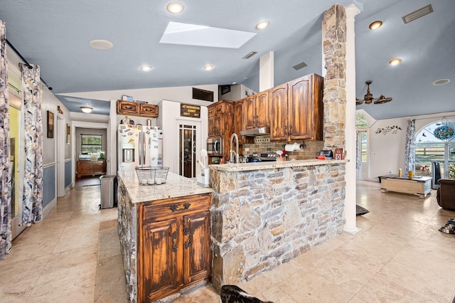 kitchen with light stone counters, vaulted ceiling with skylight, visible vents, stainless steel appliances, and under cabinet range hood