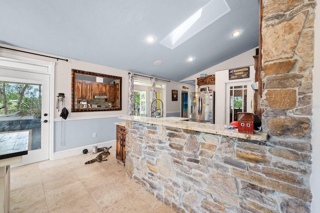 kitchen with light stone countertops, a sink, vaulted ceiling with skylight, baseboards, and stainless steel fridge with ice dispenser