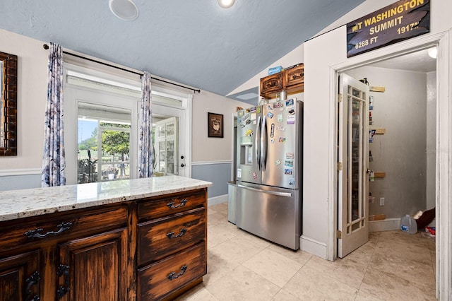 kitchen with light stone countertops, light tile patterned floors, vaulted ceiling, a textured ceiling, and stainless steel fridge with ice dispenser