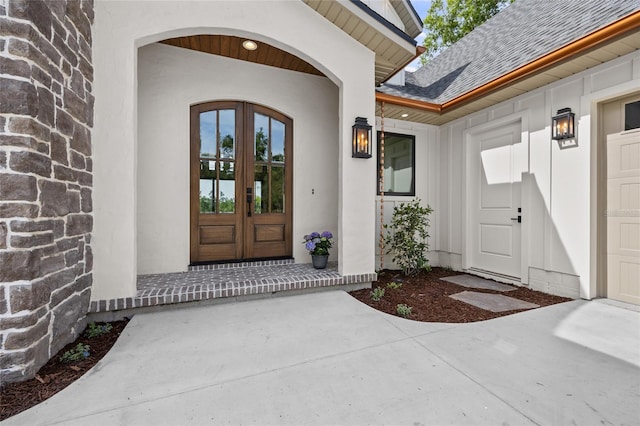 property entrance featuring french doors, a shingled roof, and stucco siding