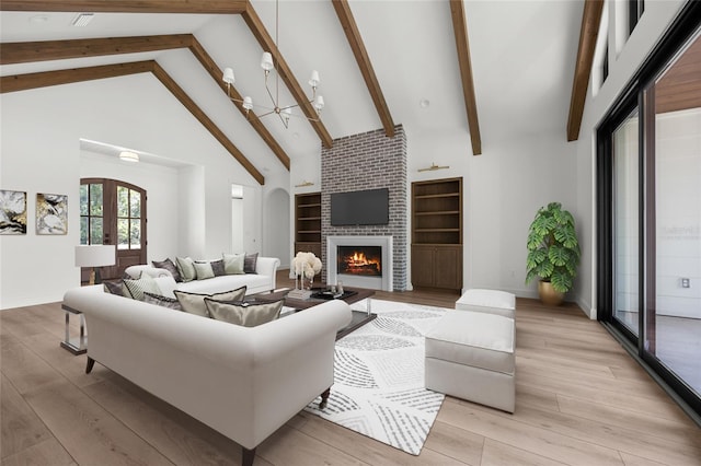 living area featuring beam ceiling, high vaulted ceiling, a large fireplace, light wood-style flooring, and baseboards