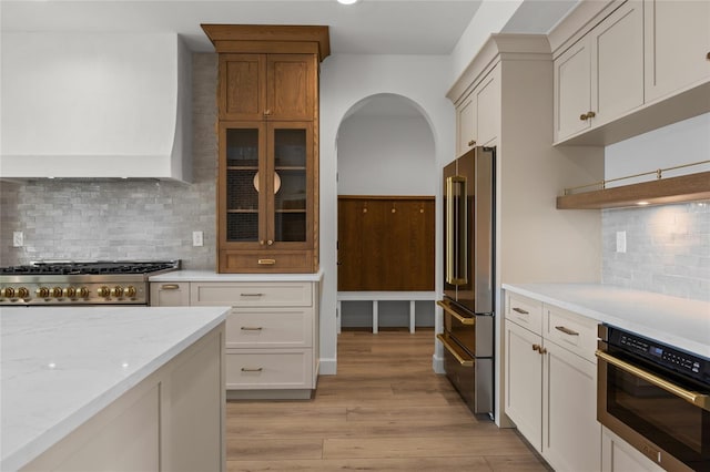 kitchen with light stone countertops, light wood-style floors, arched walkways, appliances with stainless steel finishes, and backsplash