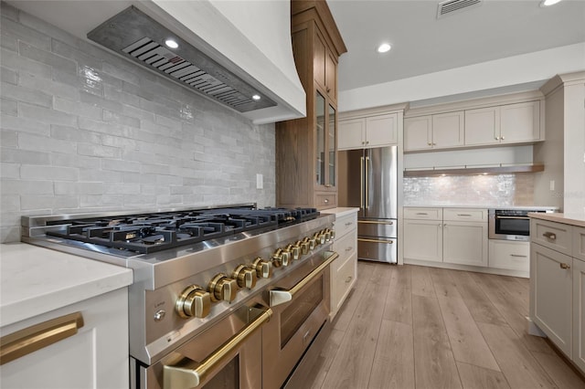 kitchen with decorative backsplash, visible vents, light countertops, custom exhaust hood, and premium appliances