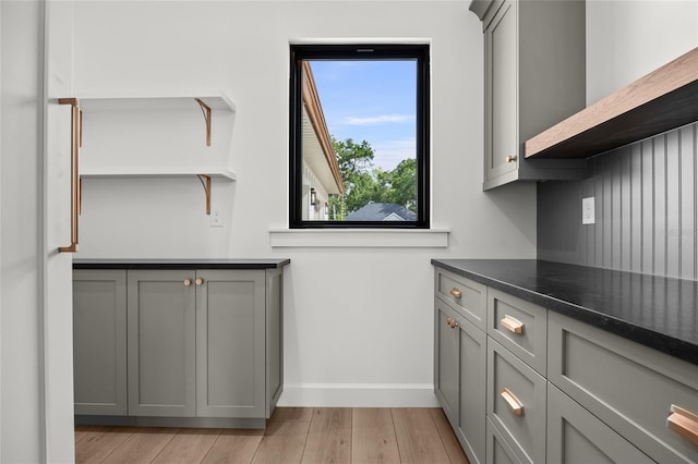 kitchen featuring gray cabinets, dark countertops, open shelves, baseboards, and light wood-style floors