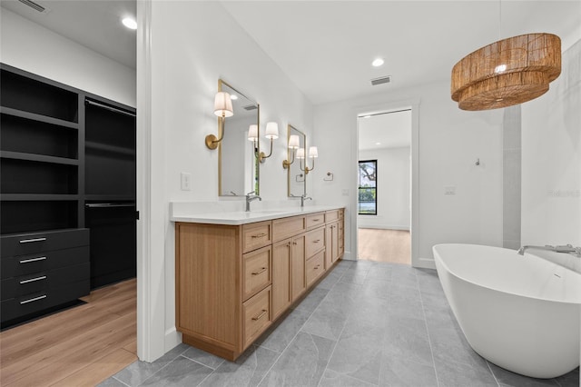 full bath with double vanity, a freestanding tub, visible vents, and baseboards