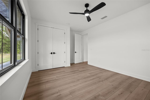 unfurnished bedroom featuring light wood-style floors, a ceiling fan, baseboards, visible vents, and a closet