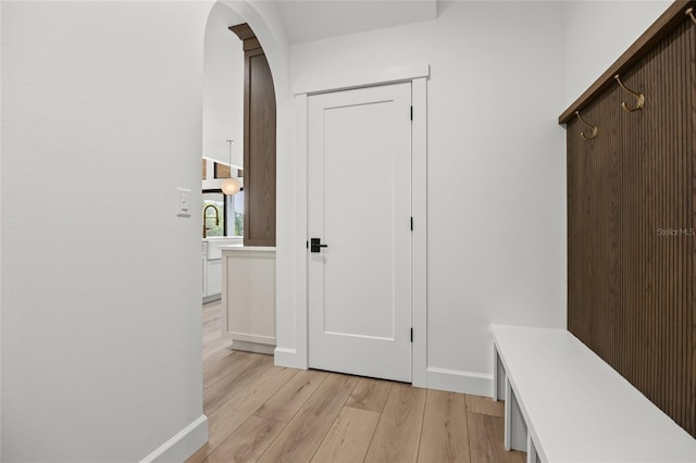 mudroom with baseboards, arched walkways, and light wood finished floors