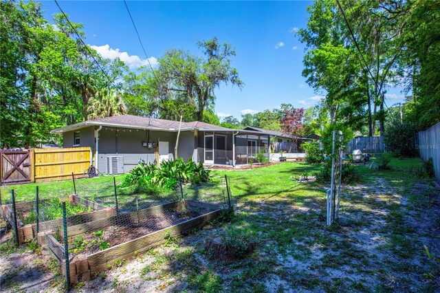 2423 NW 67th Ter, Gainesville, FL 32606 - rear view of property with a fenced backyard, a sunroom, a yard, and a vegetable garden