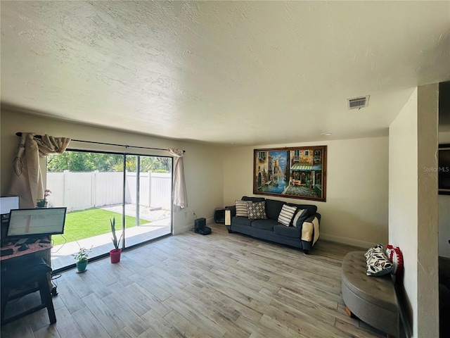 living area featuring wood finished floors, visible vents, baseboards, and a textured ceiling