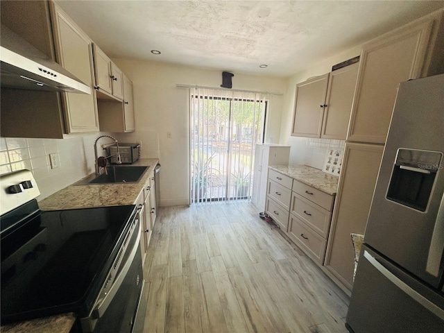 kitchen featuring a sink, stainless steel appliances, light wood finished floors, decorative backsplash, and light stone countertops