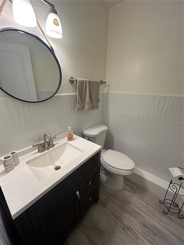 half bath with toilet, vanity, and wood finished floors