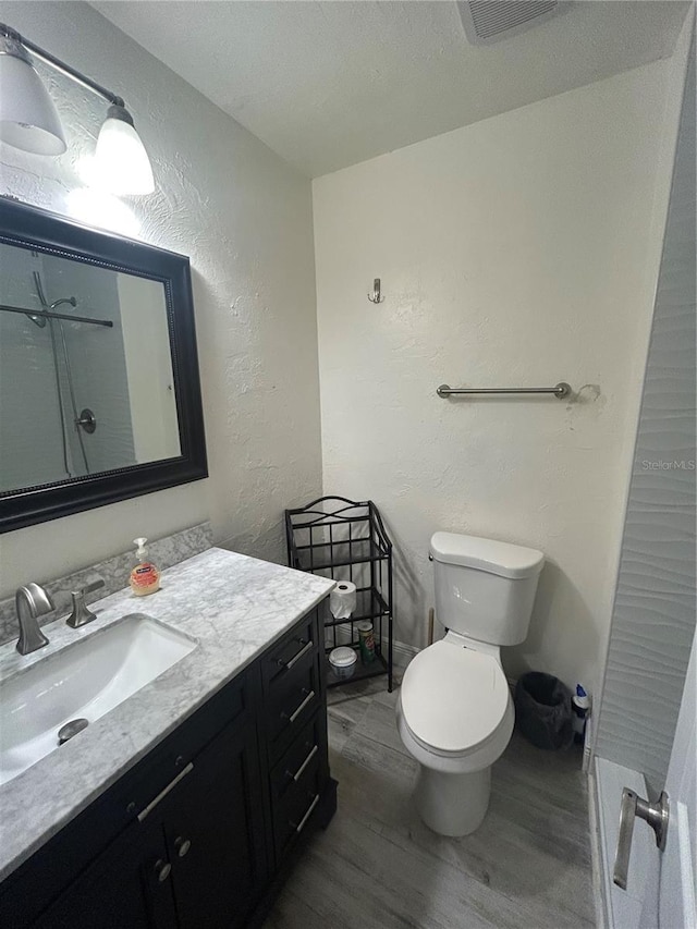 full bath with toilet, wood finished floors, visible vents, a textured wall, and vanity