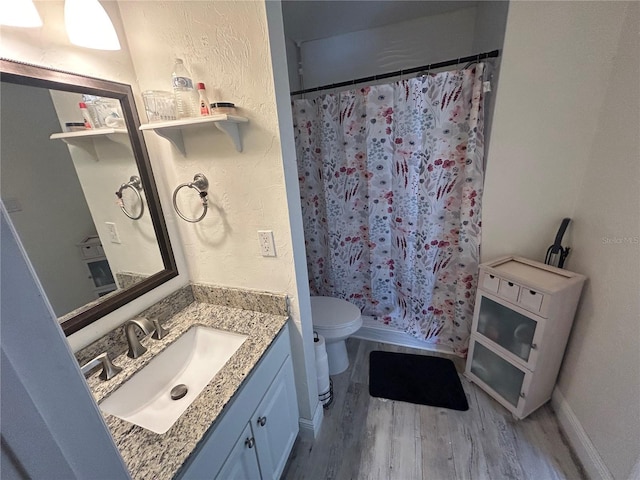 bathroom with toilet, wood finished floors, curtained shower, a textured wall, and vanity
