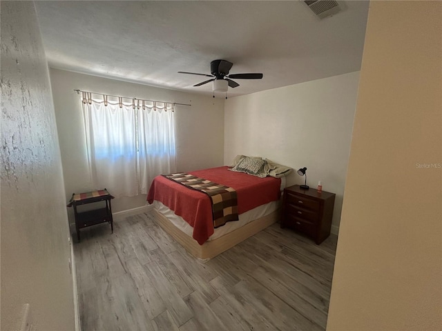 bedroom featuring baseboards, a ceiling fan, visible vents, and wood finished floors