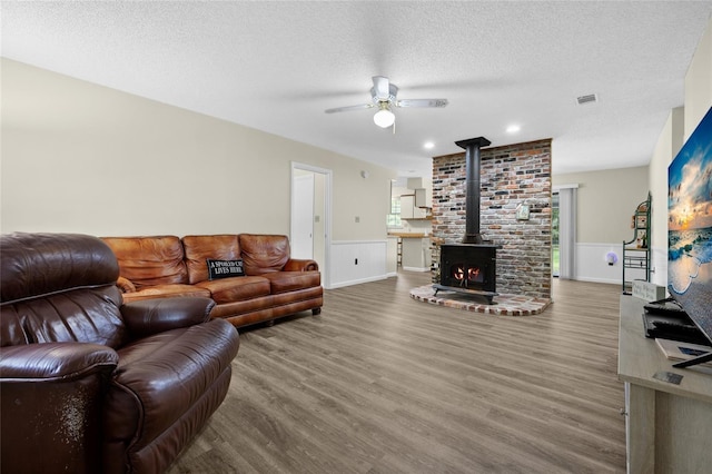 living area with a wood stove, ceiling fan, wainscoting, and wood finished floors