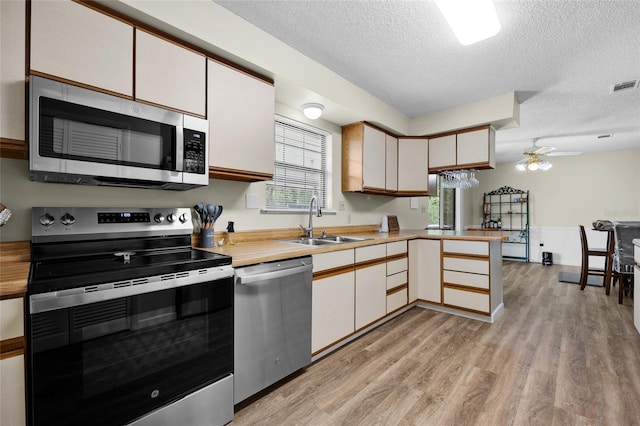 kitchen with a sink, stainless steel appliances, light wood-type flooring, light countertops, and a textured ceiling