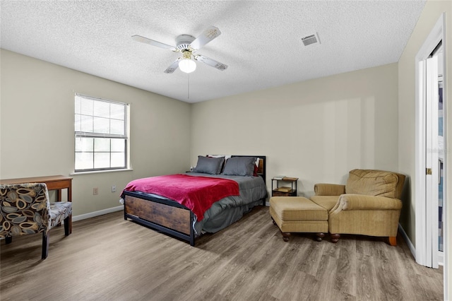 bedroom with wood finished floors, baseboards, visible vents, a ceiling fan, and a textured ceiling