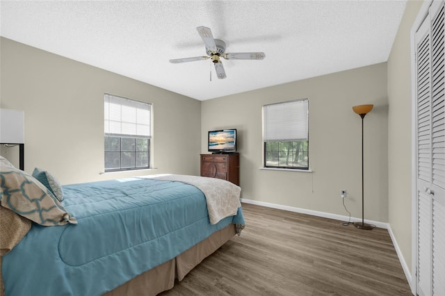 bedroom with a textured ceiling, wood finished floors, ceiling fan, and baseboards