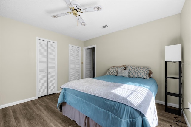 bedroom with ceiling fan, visible vents, baseboards, dark wood-type flooring, and multiple closets