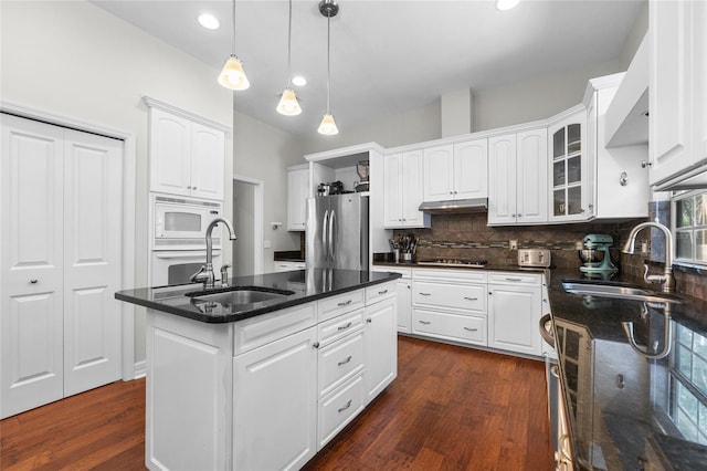 kitchen with white appliances, a sink, under cabinet range hood, dark wood finished floors, and recessed lighting
