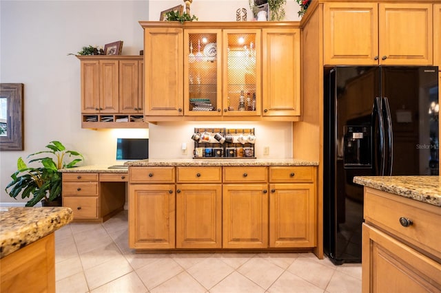 10312 SW 23rd Ave, Gainesville, FL 32607 - kitchen featuring black refrigerator with ice dispenser, light stone counters, light tile patterned floors, glass insert cabinets, and brown cabinets