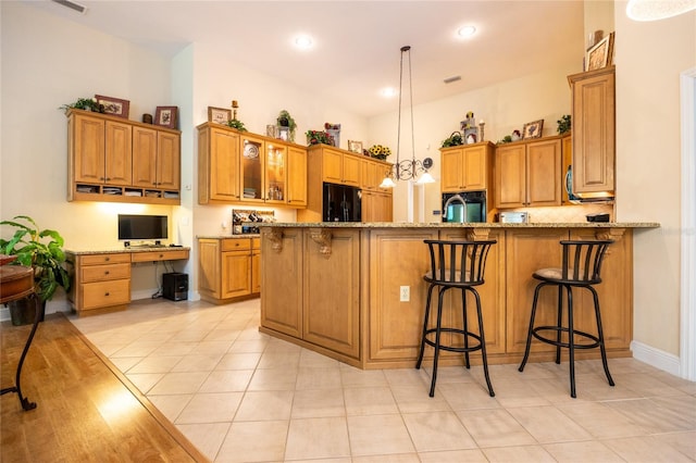 10312 SW 23rd Ave, Gainesville, FL 32607 - kitchen with black fridge, brown cabinets, light stone counters, a peninsula, and decorative light fixtures