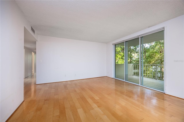 unfurnished room featuring hardwood / wood-style floors, visible vents, a textured ceiling, and expansive windows