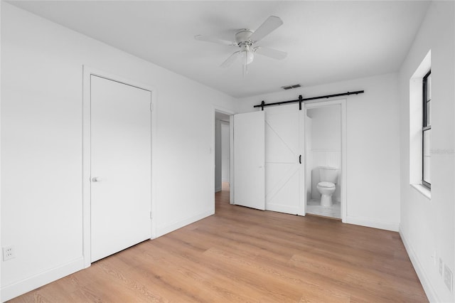 529 NE 12th Ct, Gainesville, FL 32601 - unfurnished bedroom featuring baseboards, a barn door, light wood-style flooring, connected bathroom, and a ceiling fan