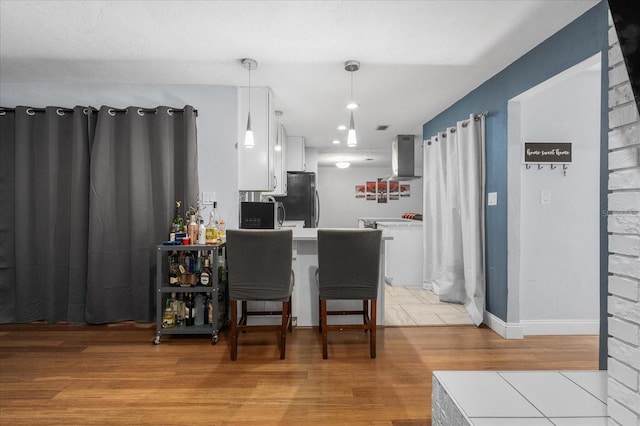 kitchen with light countertops, white cabinets, ventilation hood, freestanding refrigerator, and light wood-style flooring