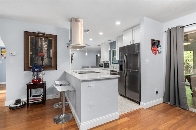 kitchen featuring a peninsula, light wood-style floors, island range hood, stainless steel fridge, and white cabinets