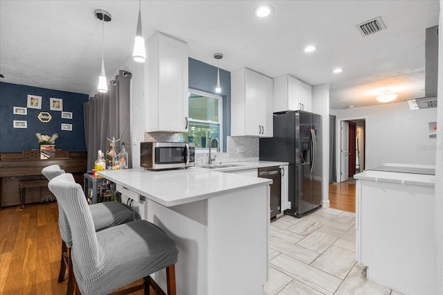 kitchen featuring white cabinets, a sink, stainless steel appliances, a peninsula, and visible vents