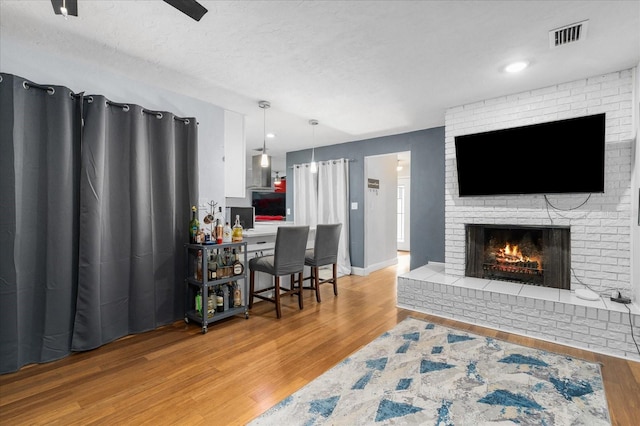 living area featuring a fireplace, a textured ceiling, baseboards, wood finished floors, and visible vents