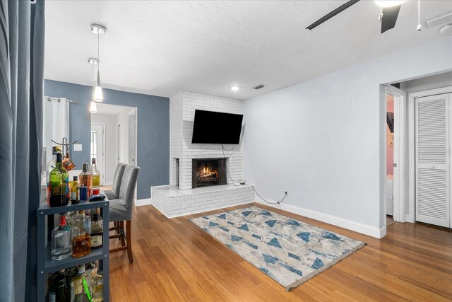 living area featuring a brick fireplace, ceiling fan, baseboards, and wood finished floors