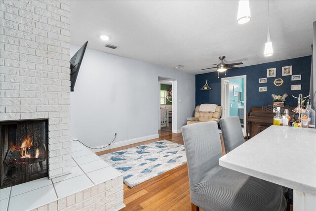 dining space with ceiling fan, visible vents, a brick fireplace, wood finished floors, and baseboards